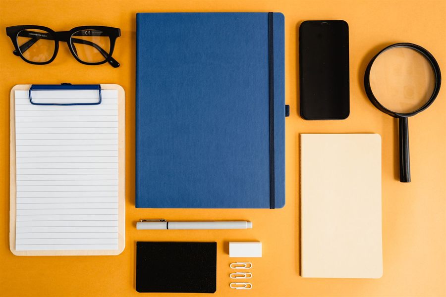 Notebooks, glasses, phone and magnifying glass laid out on a desk