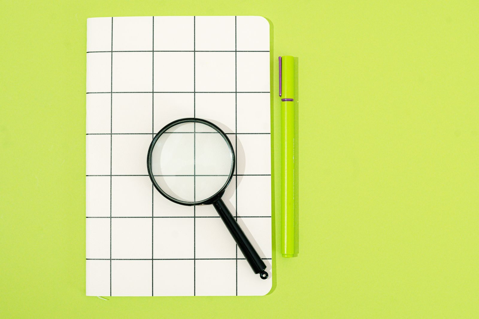 Magnifying glass on a grid notebook beside a green pen