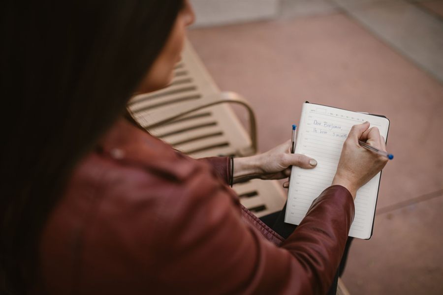 Woman writing in a notebook while sitting outdoors