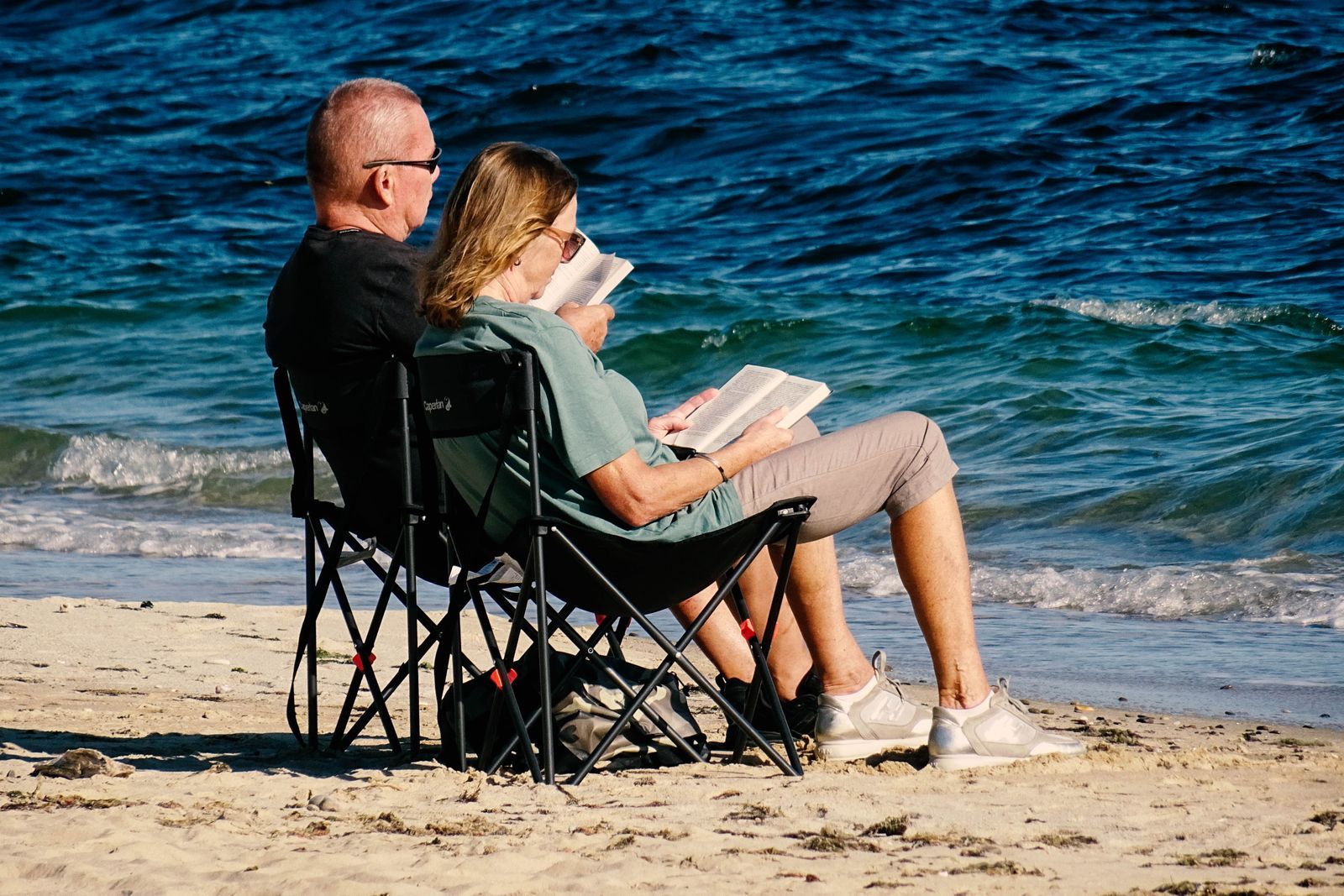 Couple reading in beach chairs at the water&rsquo;s edge, comparing cruise ship ratings and reviews